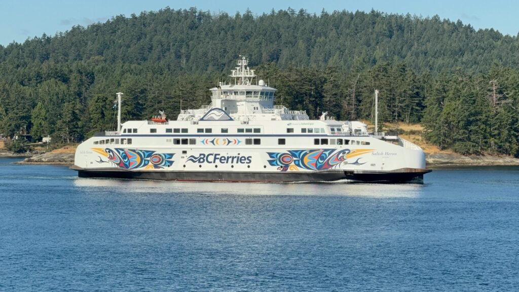 Colorful BC Ferries ship sailing through serene waters with lush forests in the background.